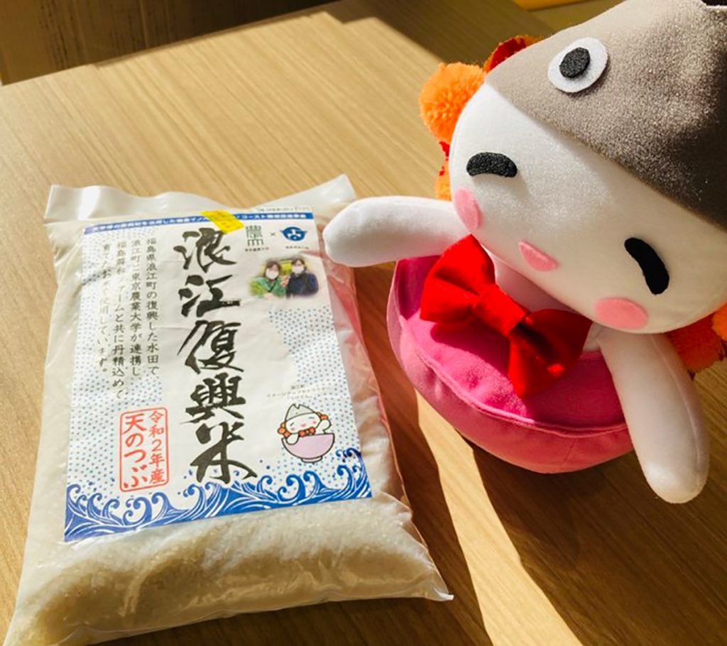 Ukedon, the “rice fairy” mascot of Namie, Fukushima Prefecture, sits next to a bag of Namie Fukko Mai (Namie reconstruction rice) in a photo posted to the town’s official Twitter account.